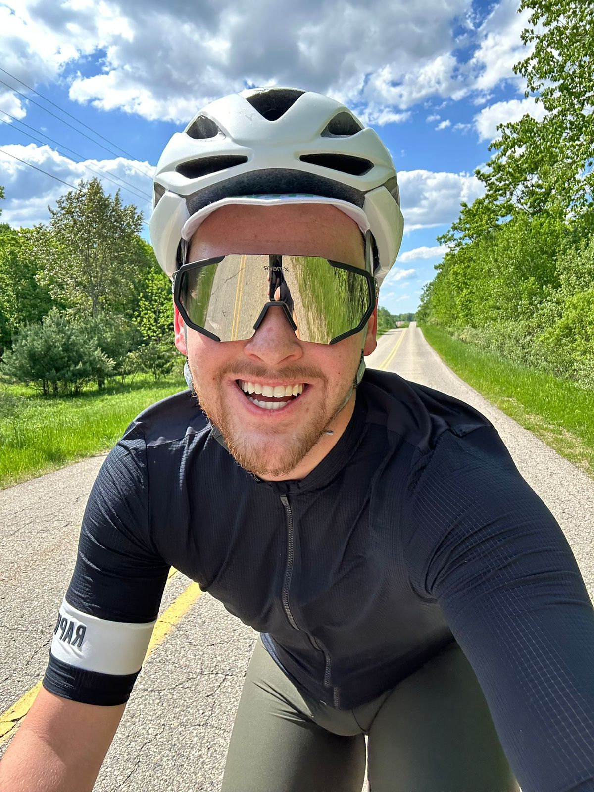 Logan Wing cycling on a sunny rural road in Michigan, wearing a helmet and reflective sunglasses