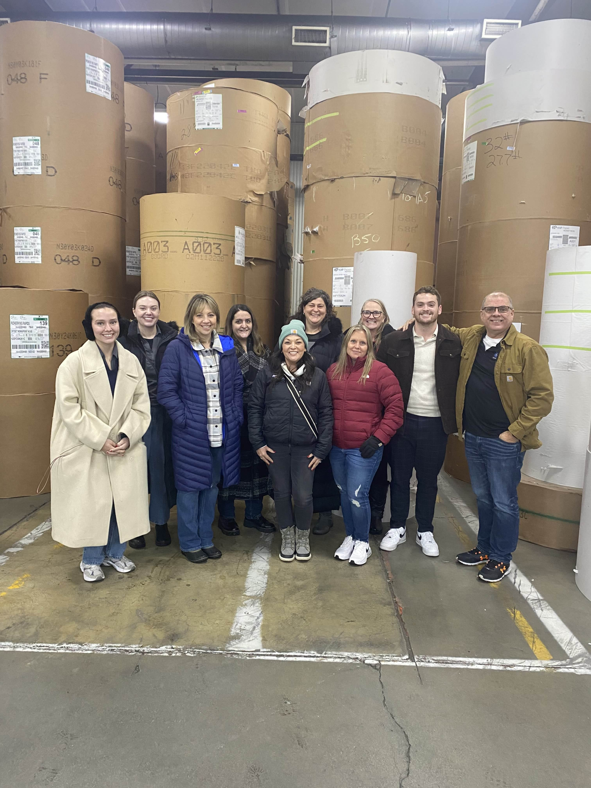 Logan Wing with a local service group standing in front of large paper rolls during a Rotary community visit.